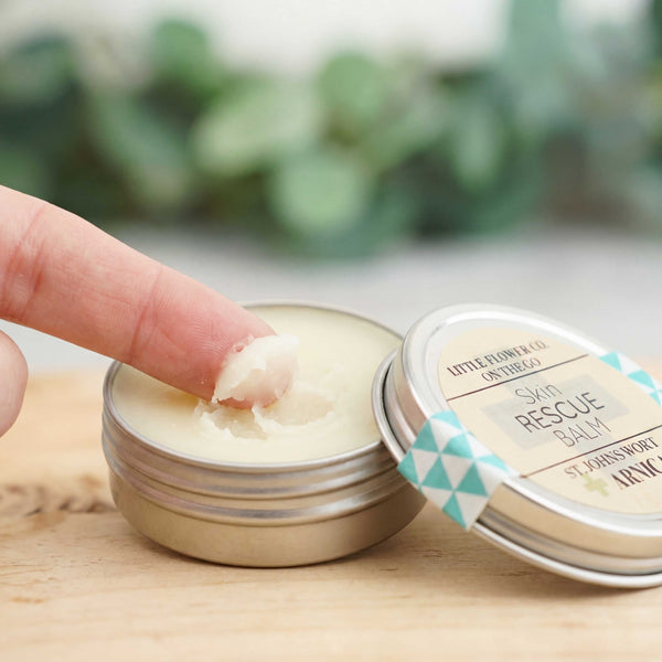 the little flower soap co skin rescue balm 1 oz tin open and someone is dipping finger in to use